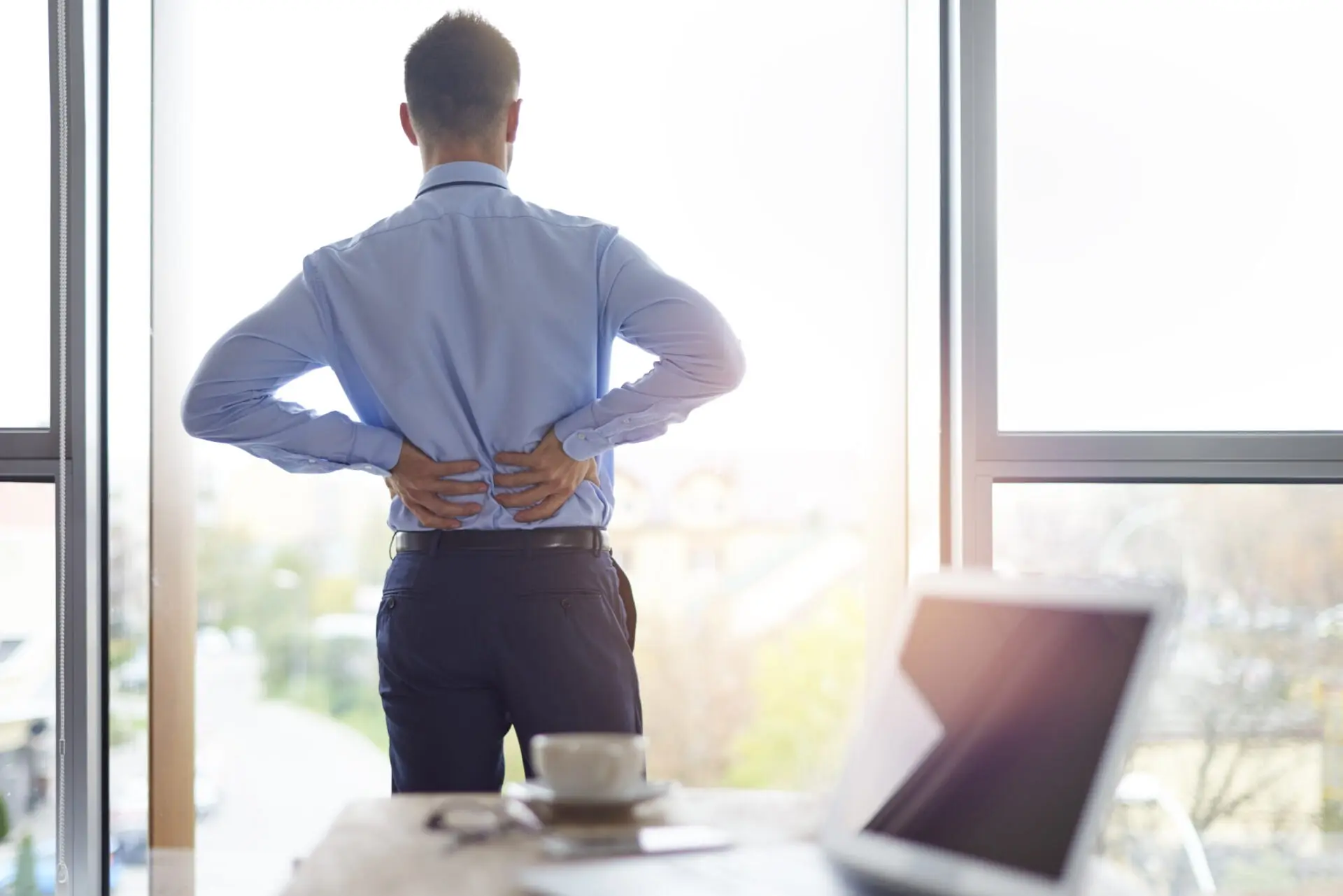 man in office attire standing holding his low back in pain