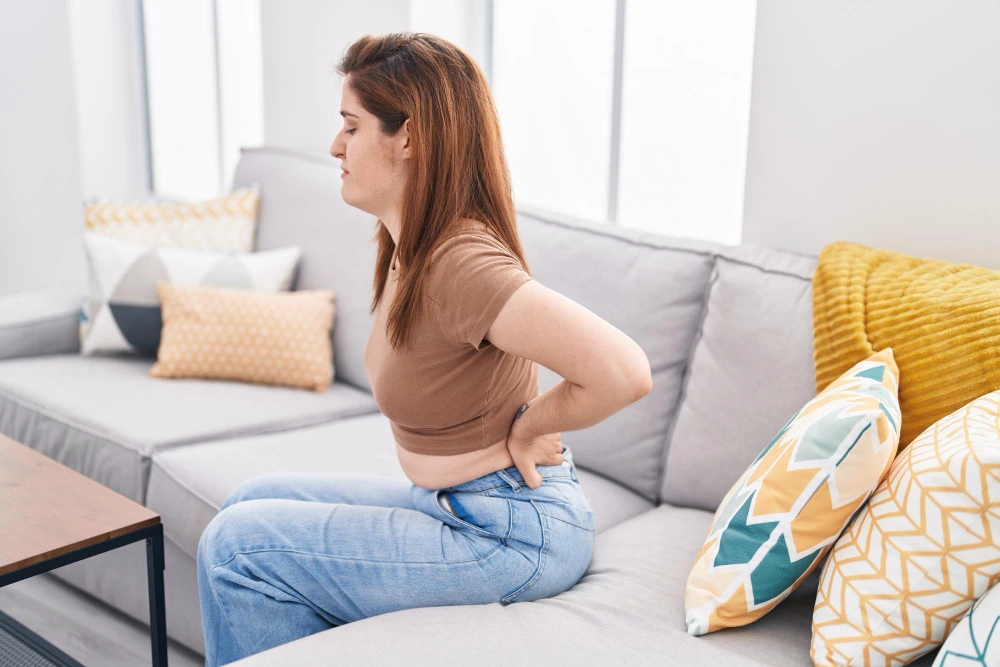 female sitting on couch holding her low back in pain