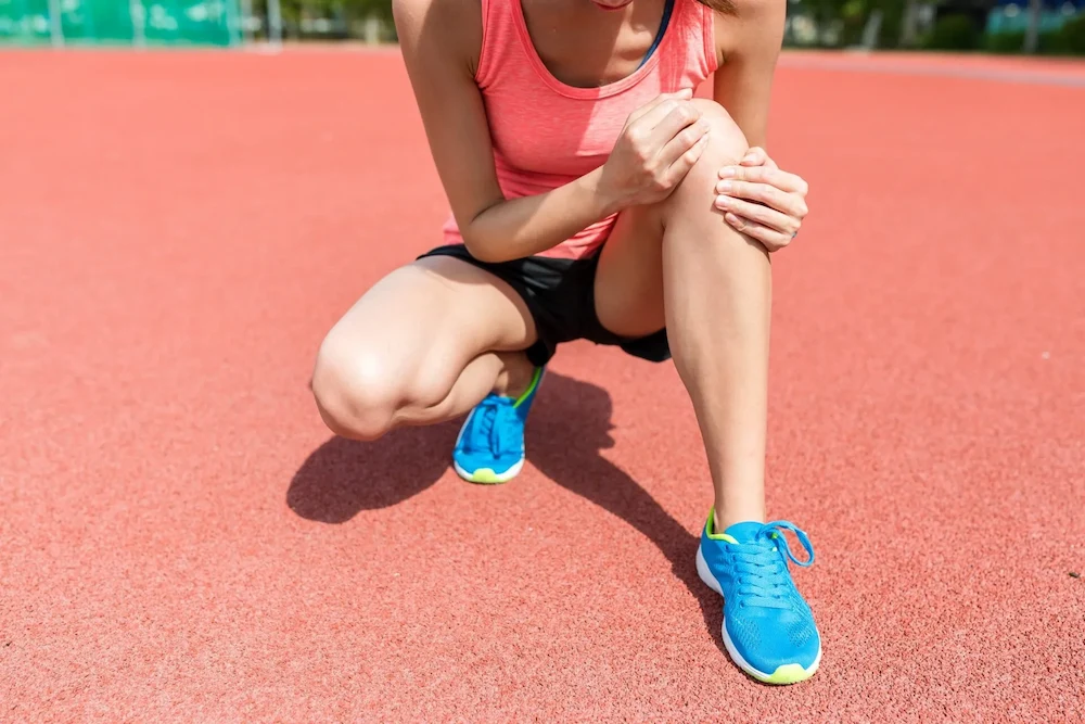 female holding her knee in pain on track