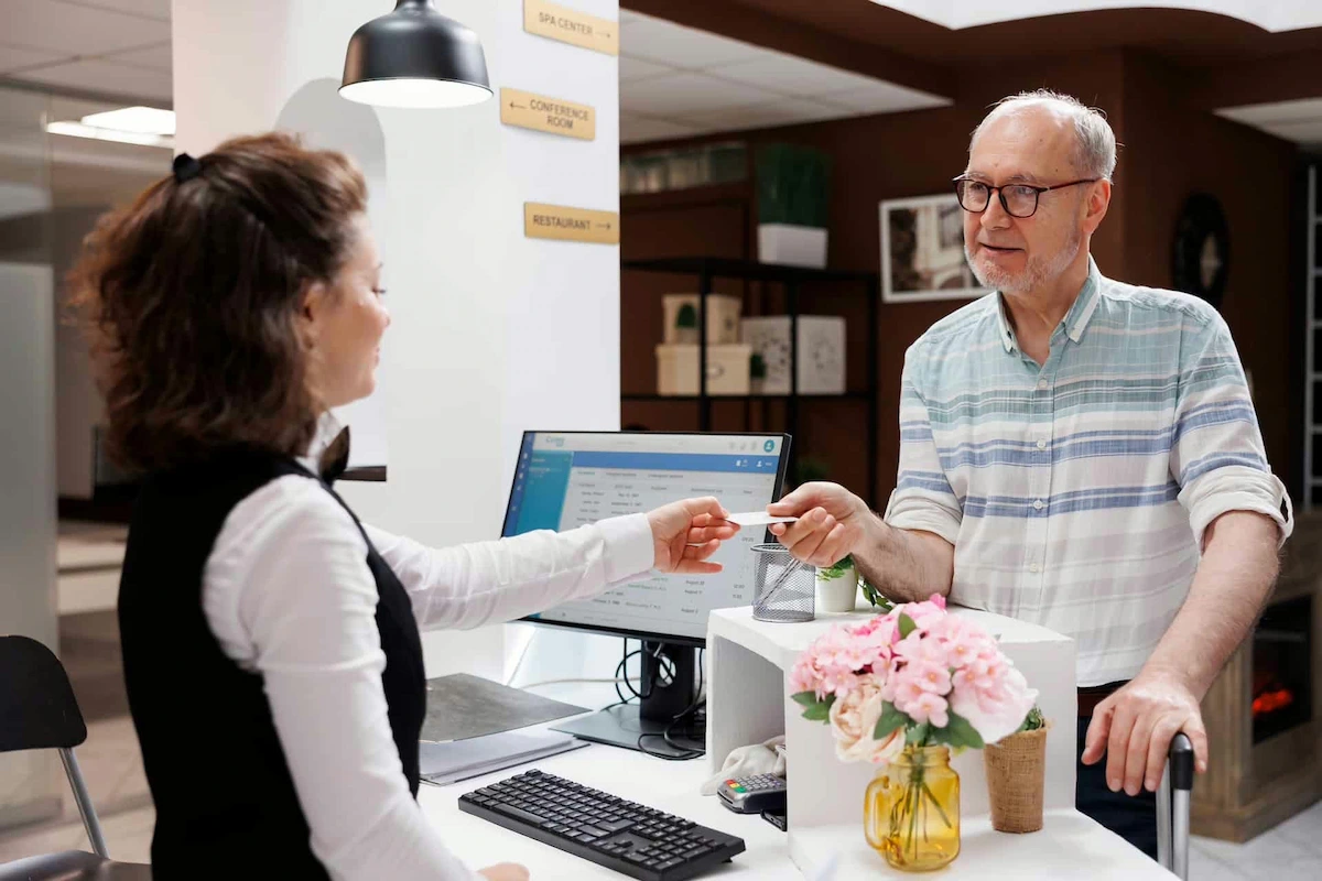 elderly man handing his payment information to a front desk assistant