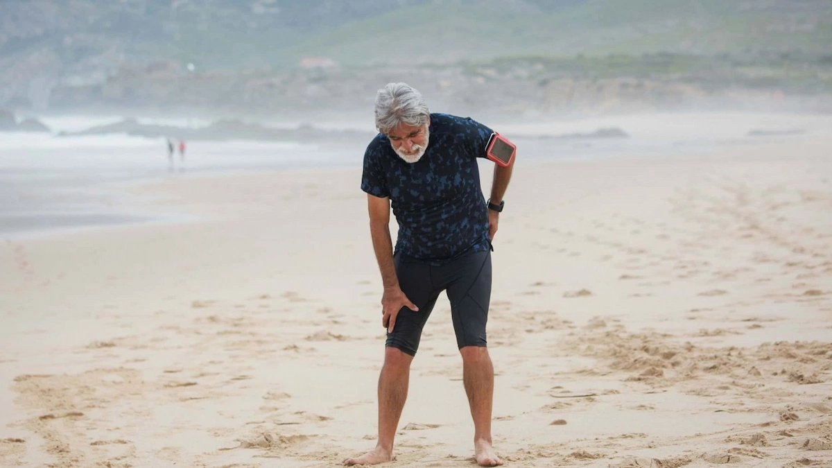 elderly man hunched over in pain on beach
