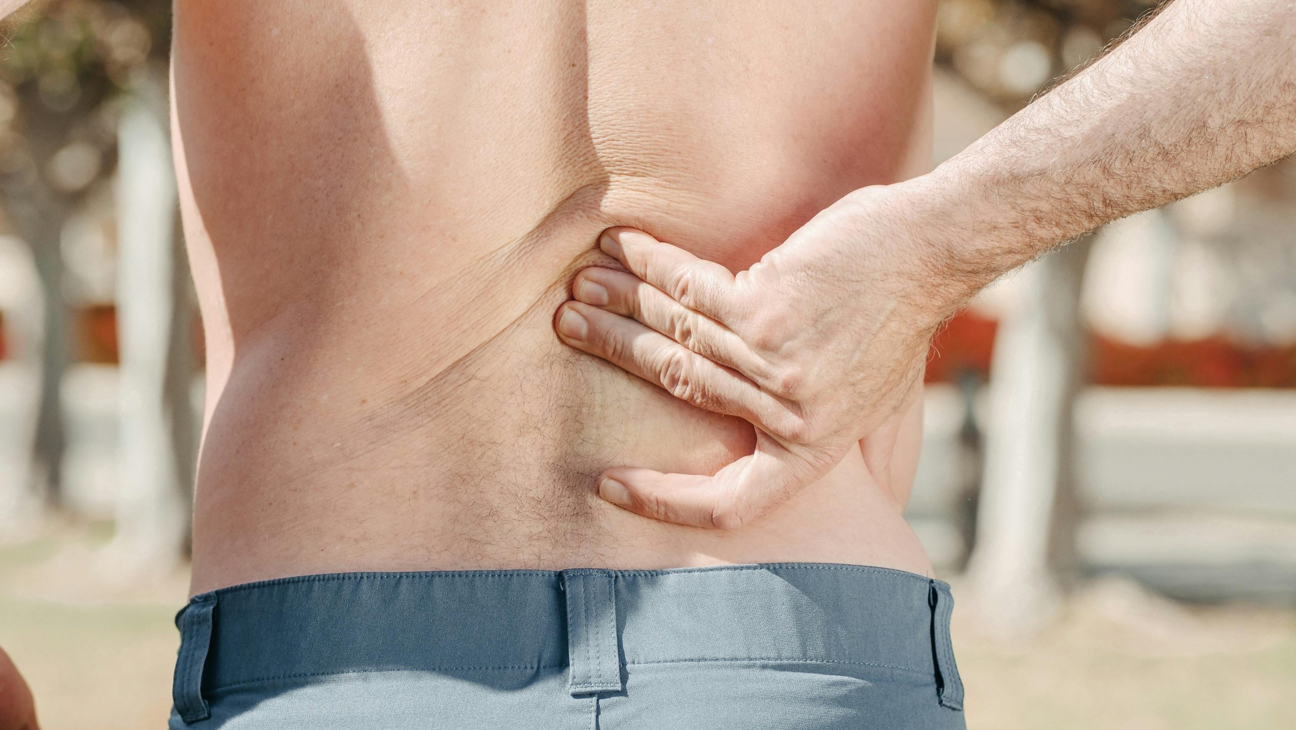 A person from behind, holding their lower back with one hand, indicating back pain.