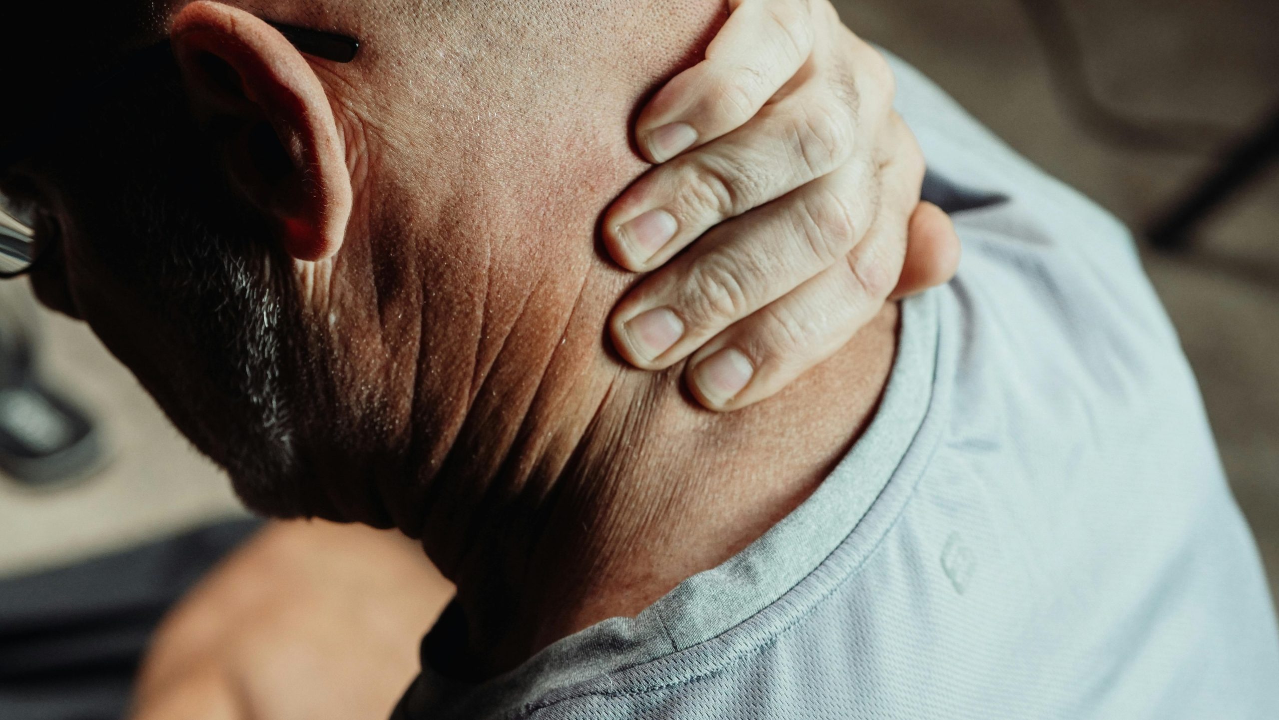 Close-up of a person's hand grasping the back of their neck, seen from behind.