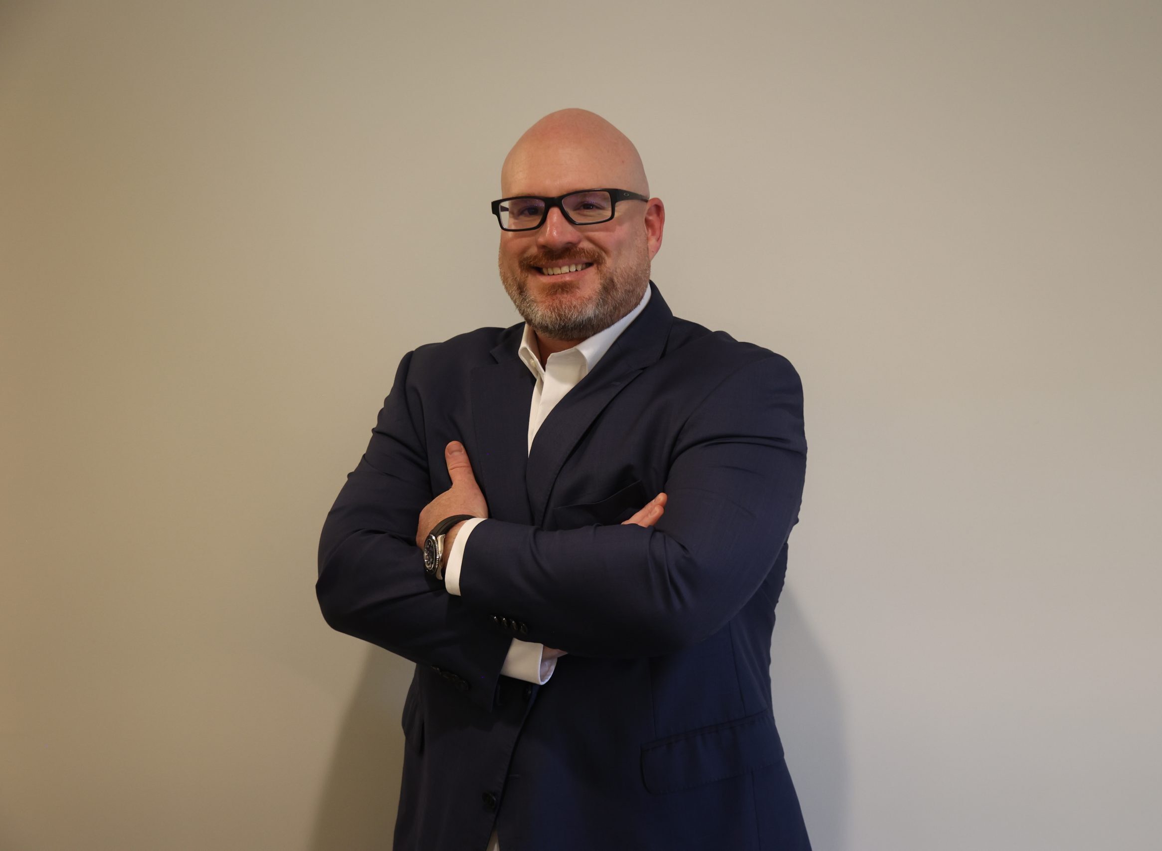 Bald man with beard and glasses wearing a suit, arms crossed, smiling at the camera.