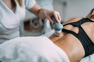 A therapist uses a handheld device with gel on a patient's lower back.