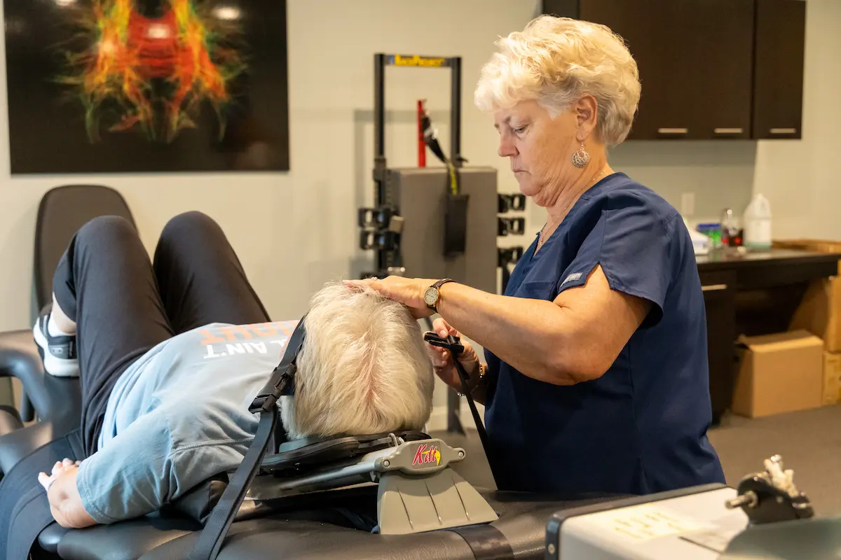 A healthcare professional helps a patient lying on a table with a neck traction device in a clinic.