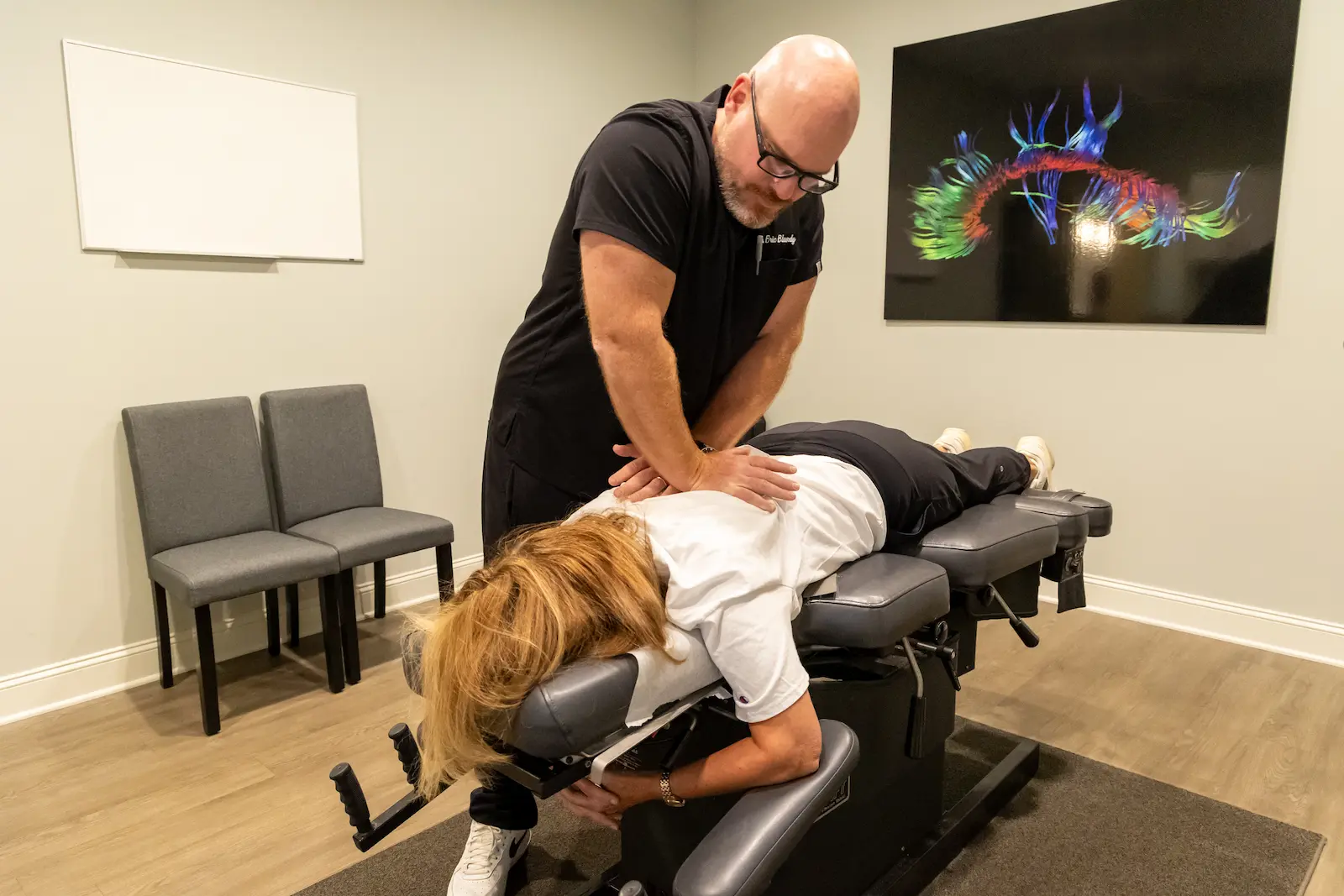 A male chiropractor adjusts a female patient's back on a chiropractic table in a clinic.