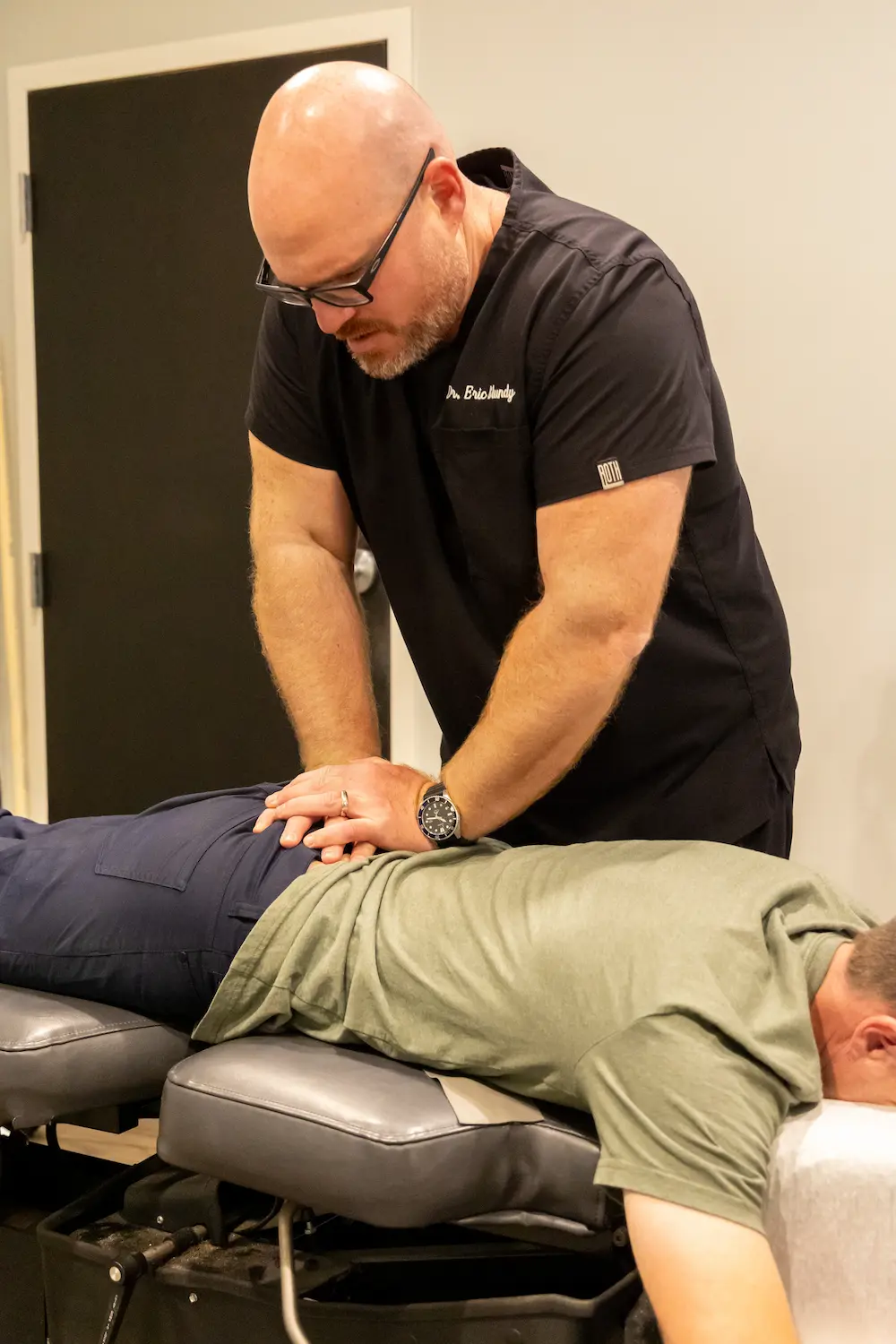A chiropractor, Dr. Eric Handy, performs a lower back adjustment on a patient lying face down on an examination table.