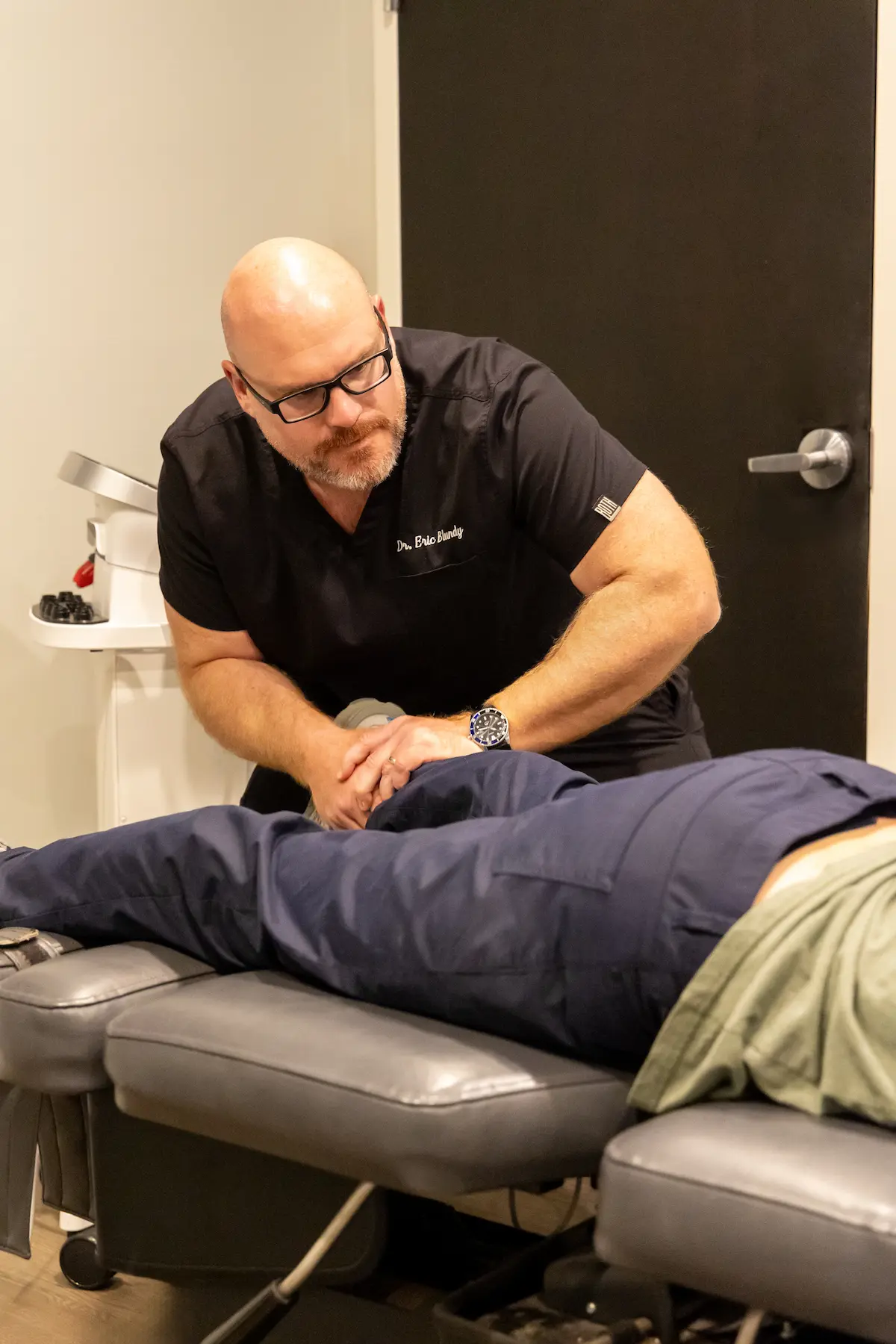A chiropractor, Dr. Eric Blundy, adjusts a patient's lower back on a chiropractic table.