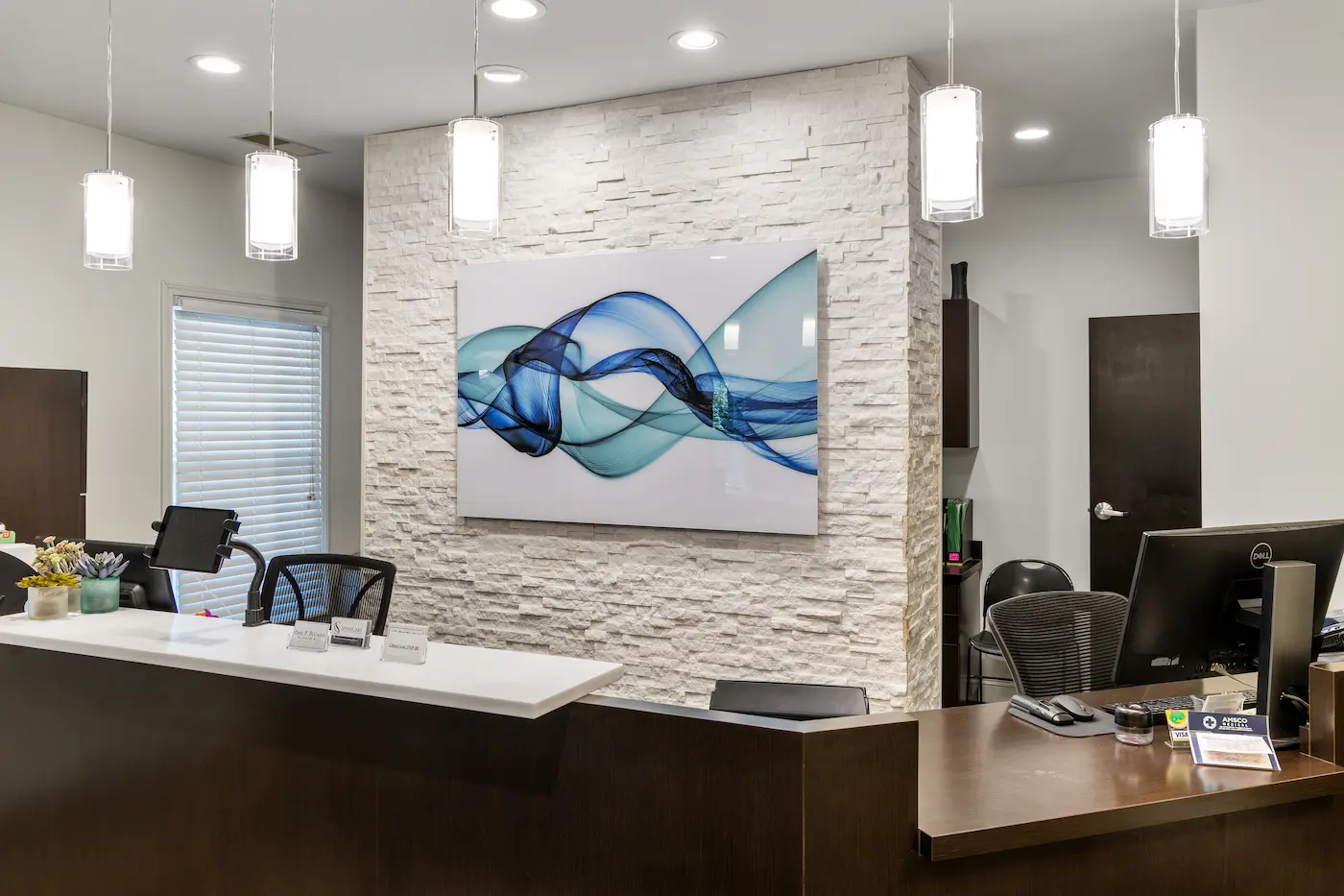 A modern reception area with a dark wood desk, white stone accent wall, and a large abstract artwork with blue and teal wavy lines.