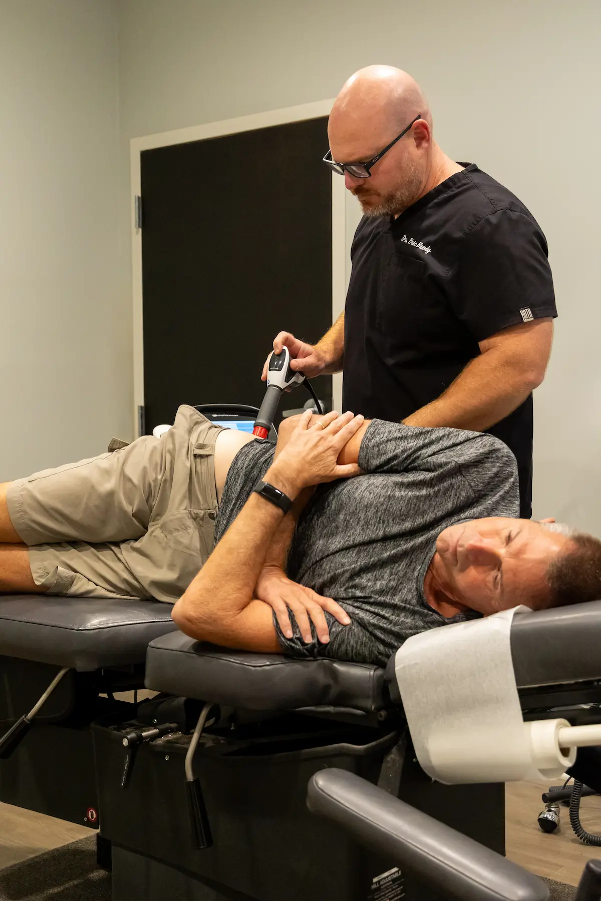 A doctor uses a handheld device on a patient's lower back while the patient lies on a medical table.