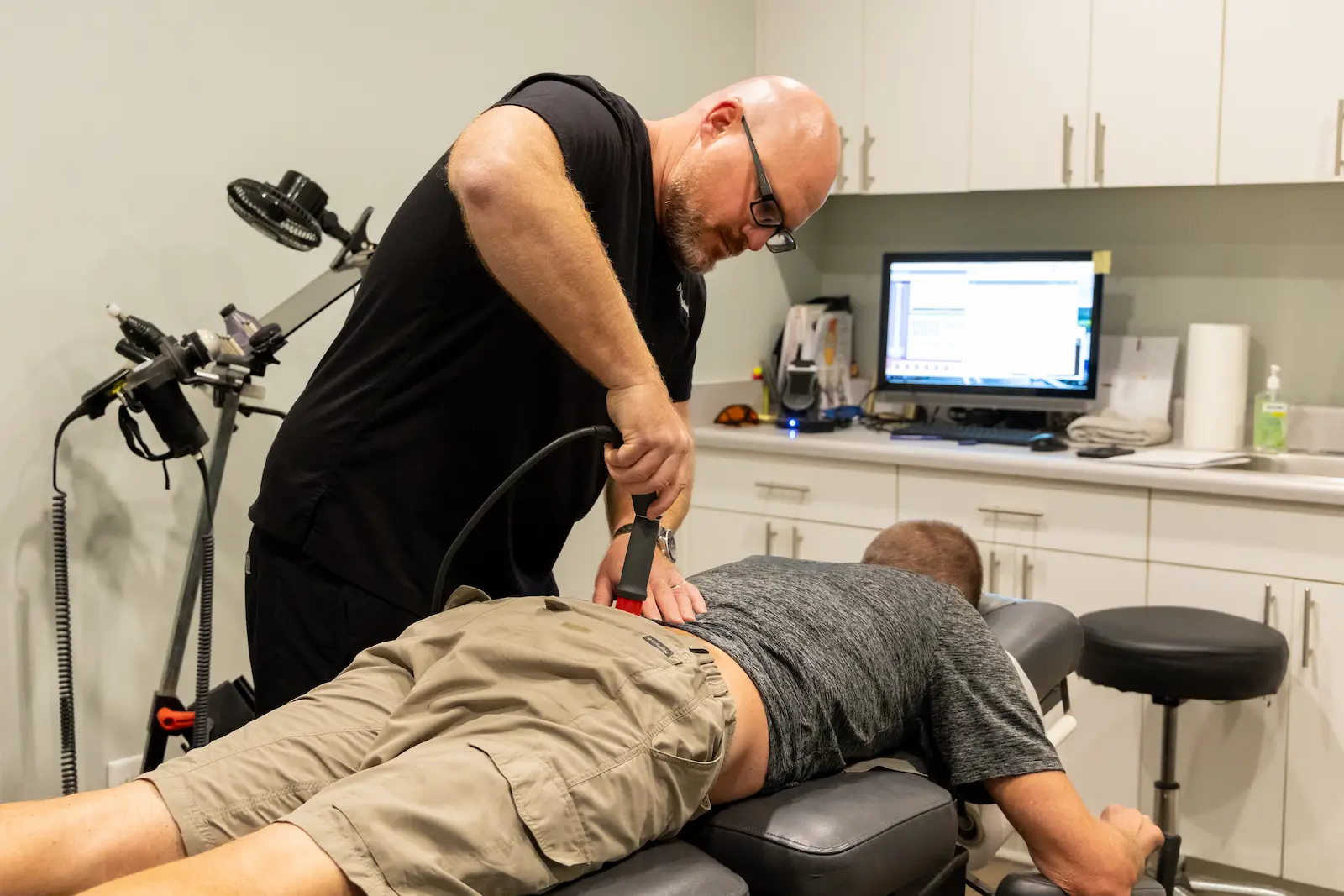 A practitioner treats a patient's lower back with a medical device on a treatment table.