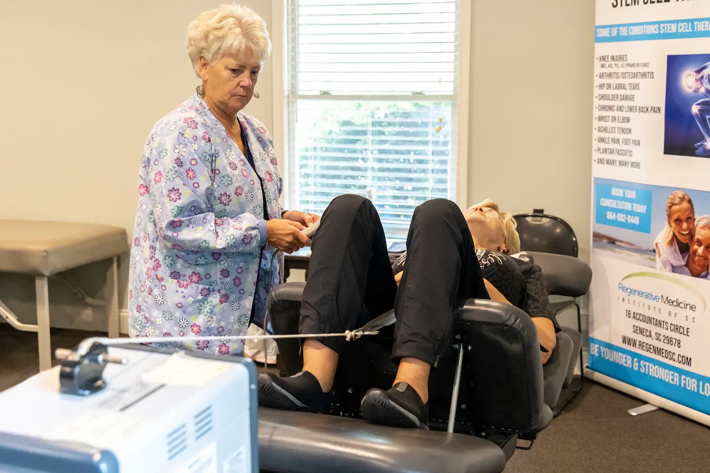 A medical professional assists a patient receiving leg therapy in a reclined chair, with a stem cell therapy banner in the background.